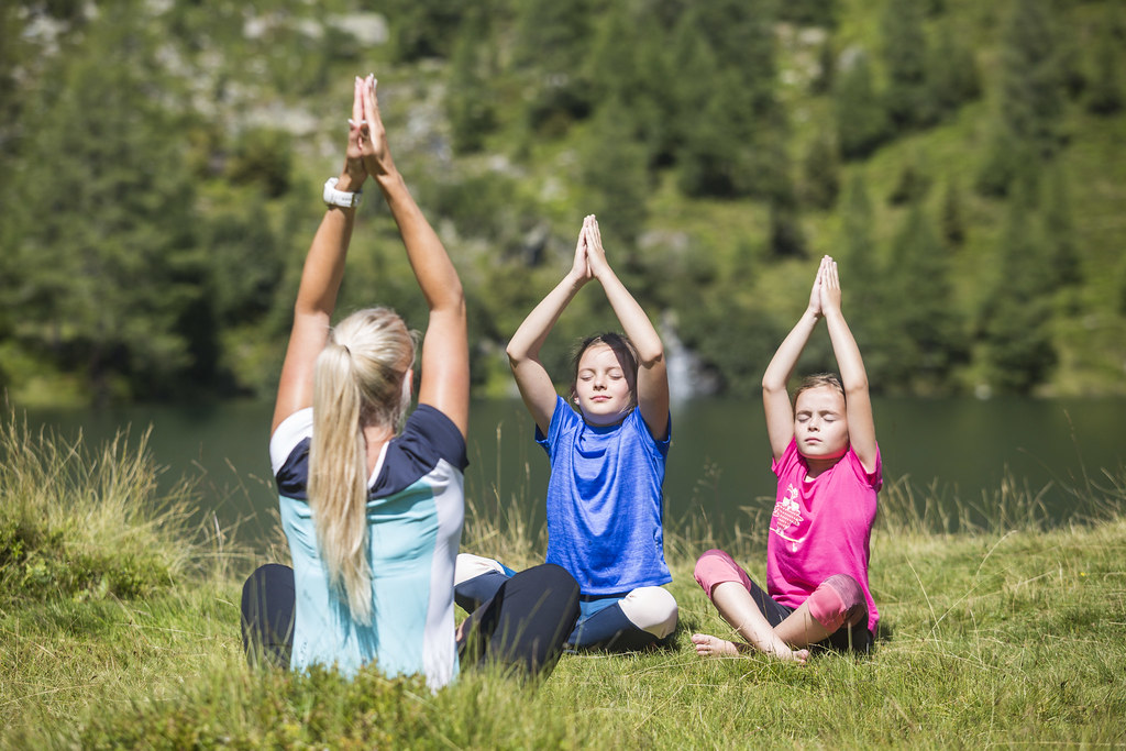 Eine Frau und zwei Kinder machen Yoga am Wirpitschsee in der Wiese.
