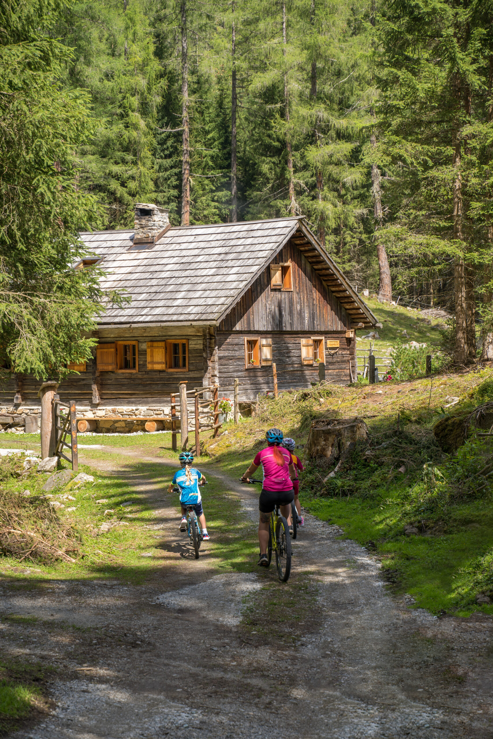 Zwei Radfahrerinnen fahren auf eine Almhütte zu im Sommer